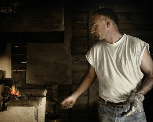A homeowner scooping ash and brushing the inside of a wood stove firebox
