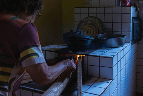 A person carefully removing ceramic logs from a gas stove to clean the burner