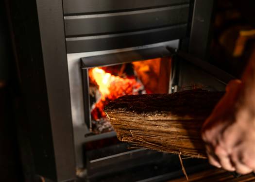 A homeowner lighting a wood stove with kindling and dry logs